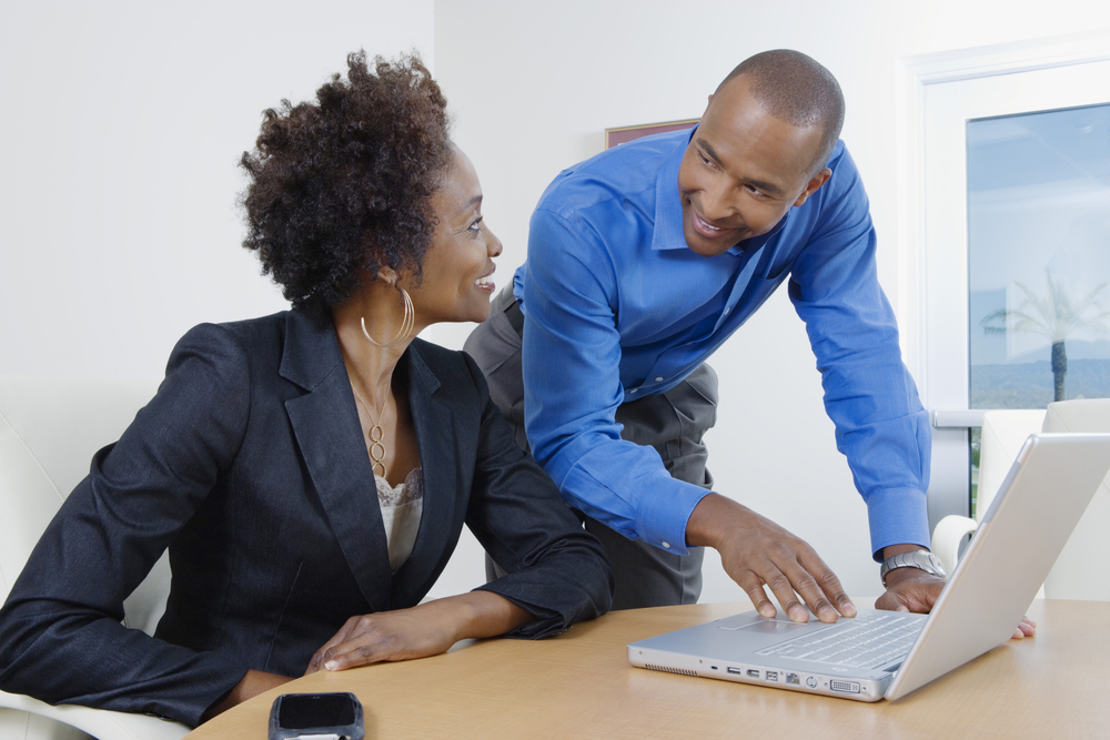 A man in a blue shirt and a woman in a blazer reviewing something on a laptop together