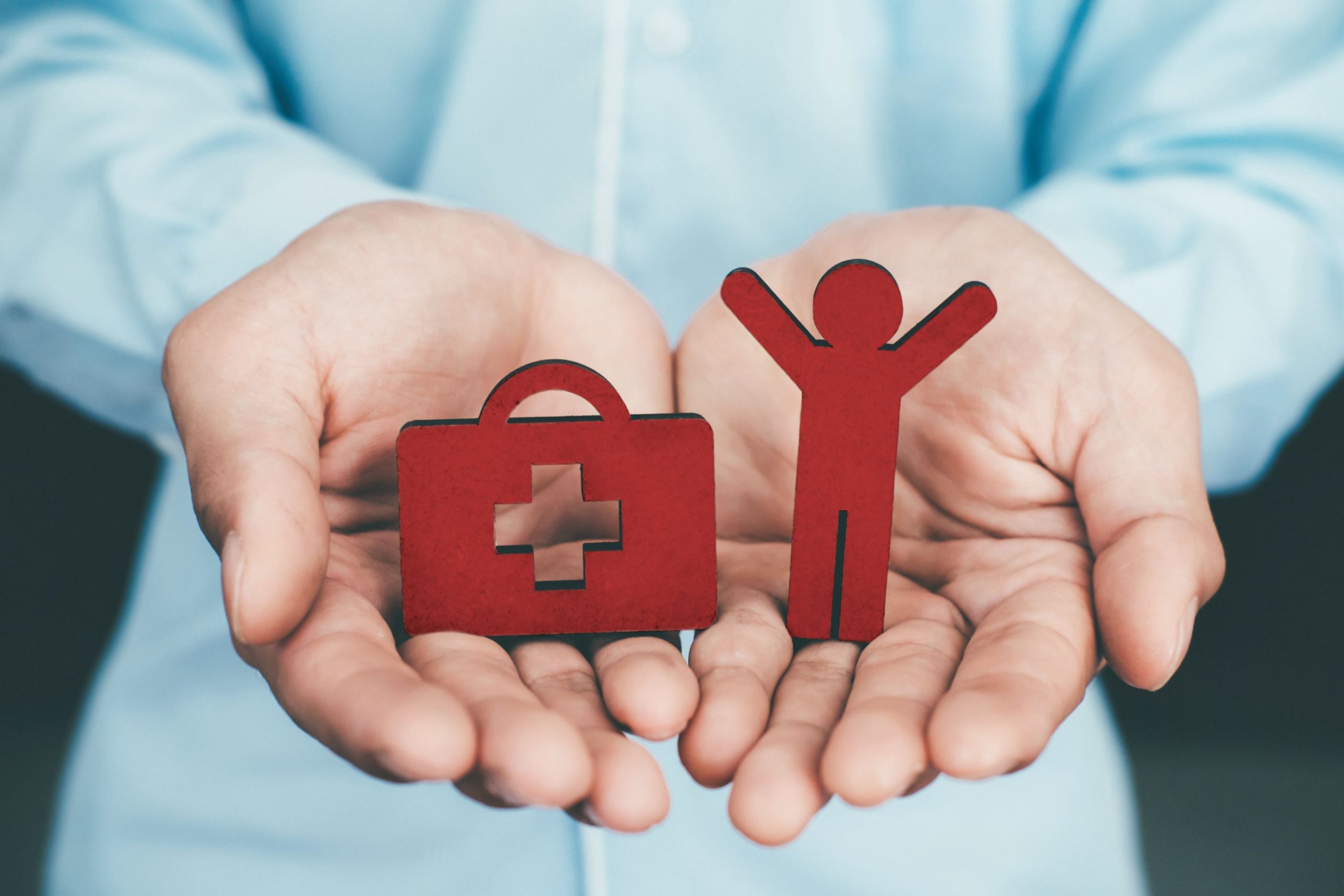 Open hands holding red cut-outs of a first-aid kit and a person