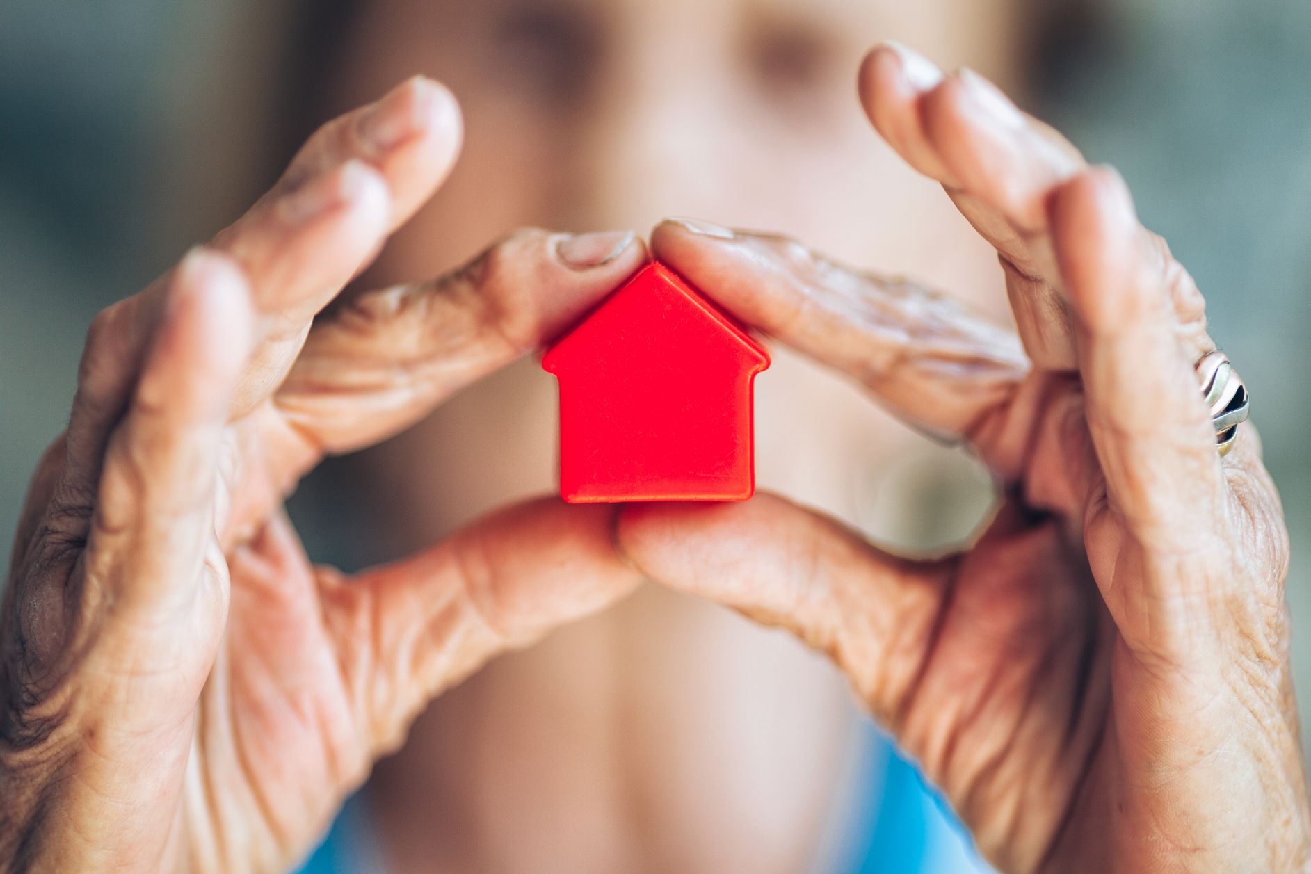 Weathered hands holding a small red model house