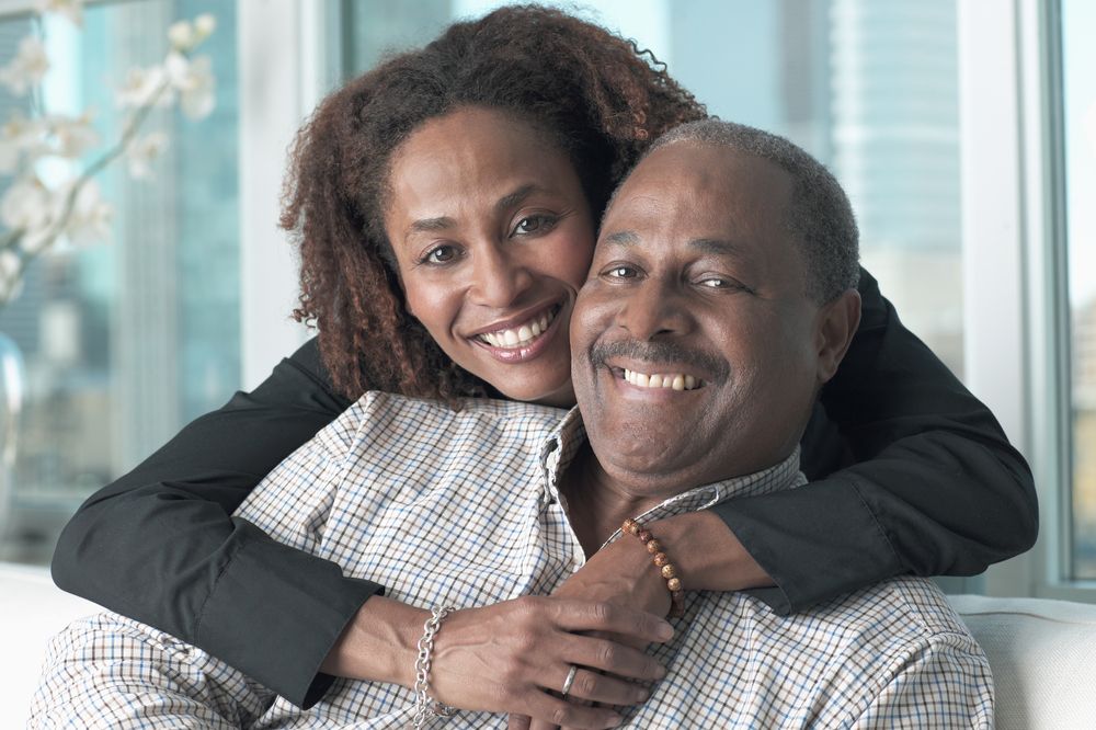 A woman hugging an older man from behind, both smiling