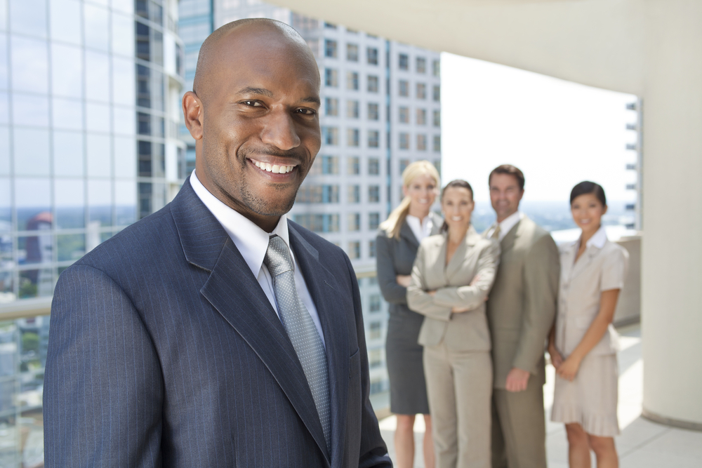 A smiling man in a suit in front of colleagues on a city terrace
