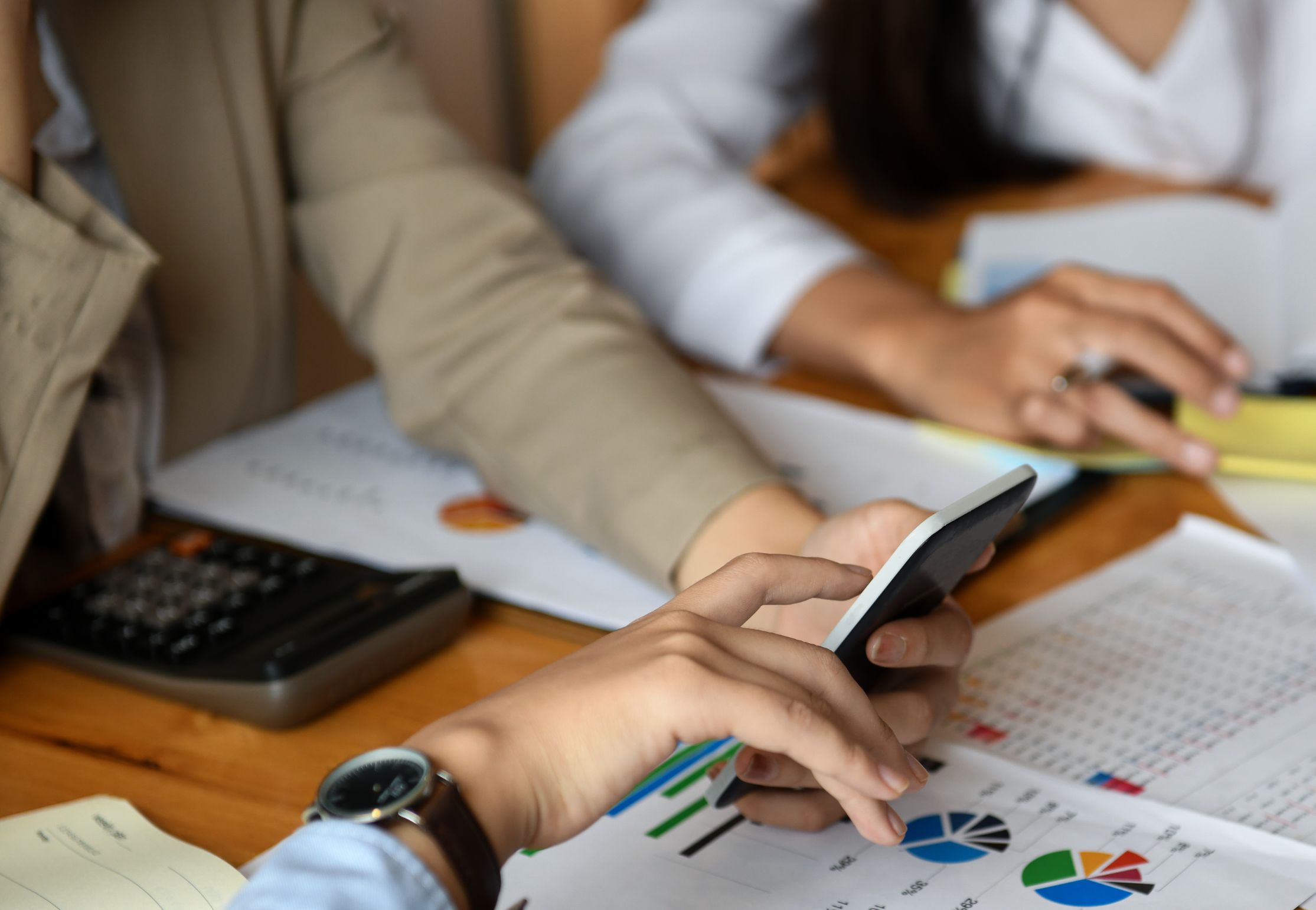 Colleagues' hands working with a calculator, phone and printed charts