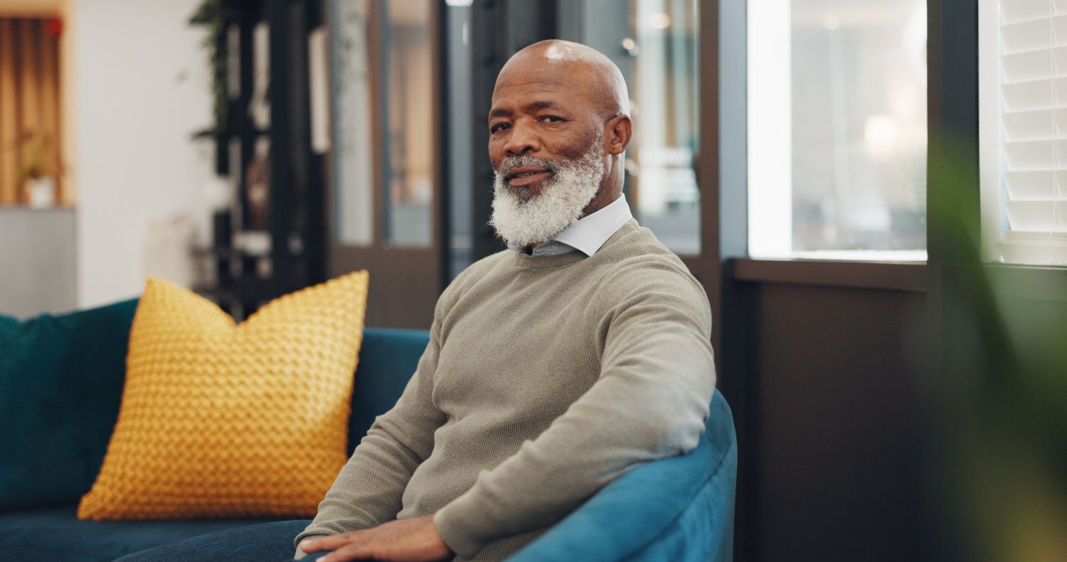 An older man with a grey beard seated on a sofa