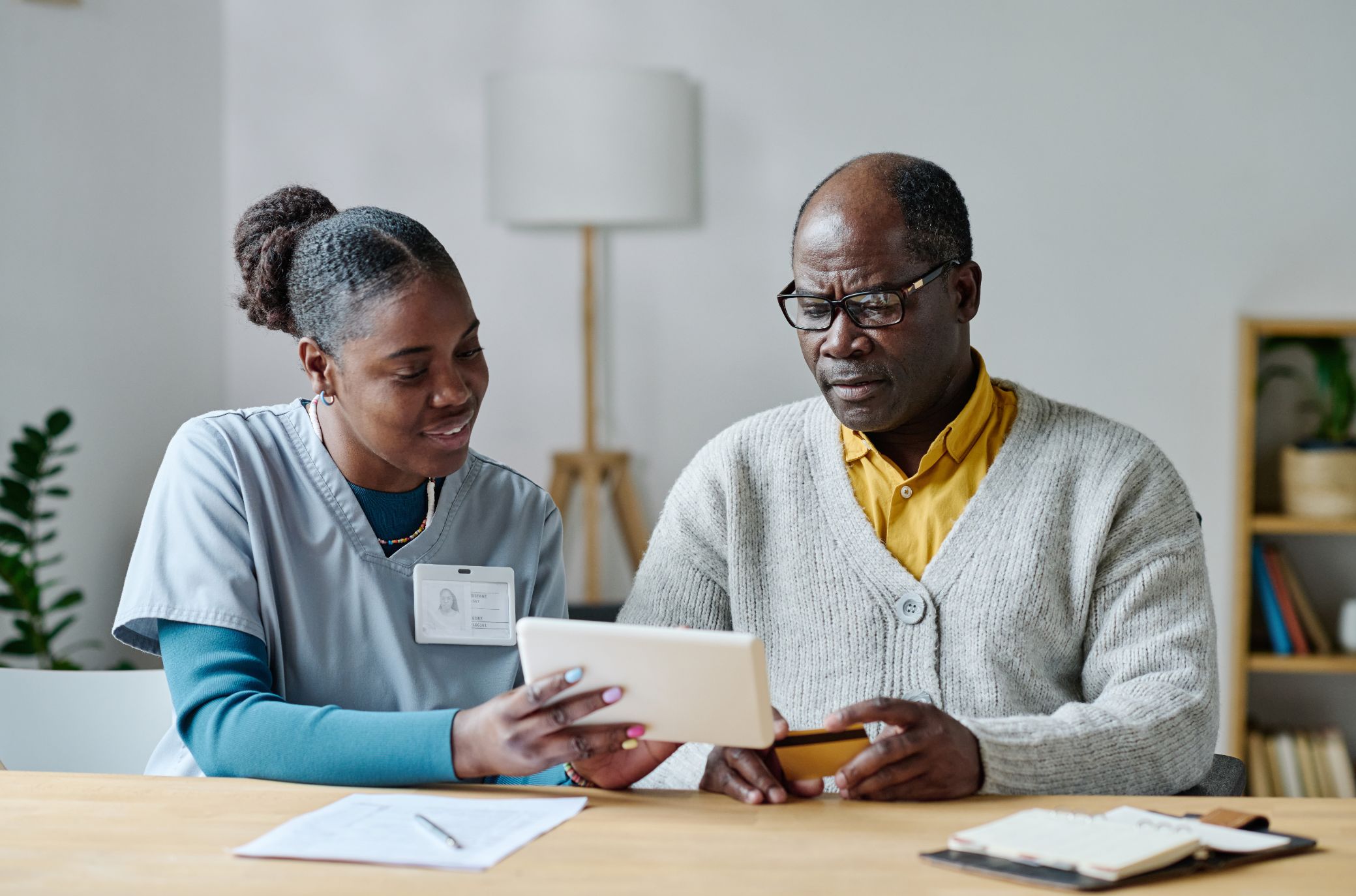 A young care worker helping an older man with a tablet at a table